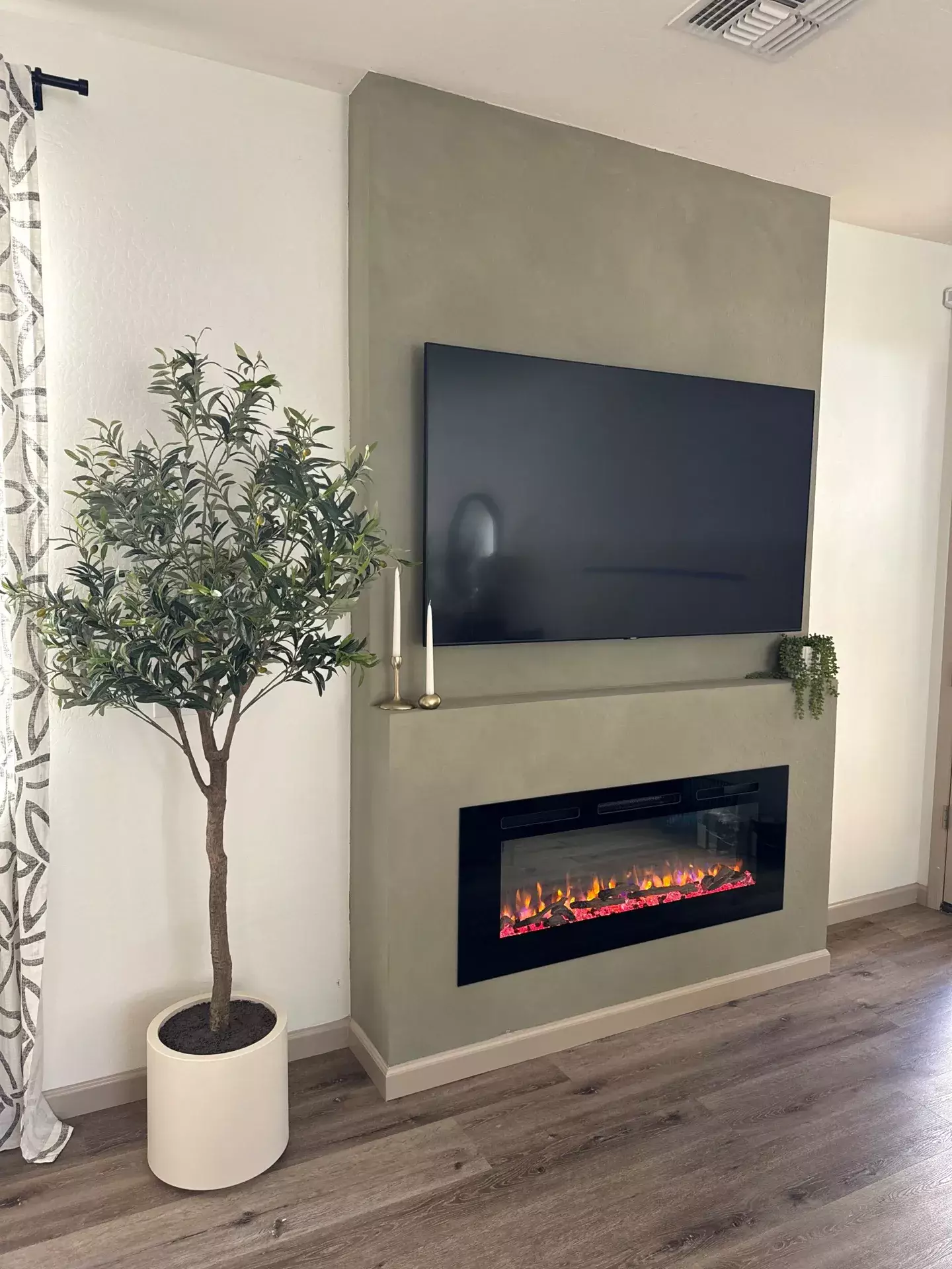 Modern media wall with mounted TV and built-in electric fireplace, featuring green limewash finish and minimalist decor.