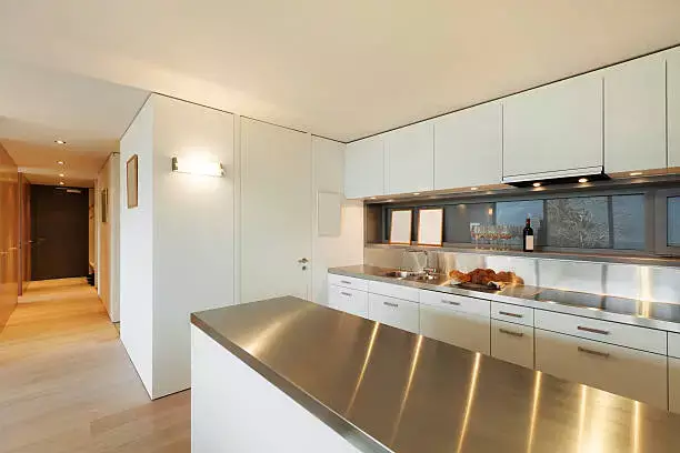 A modern kitchen featuring sleek stainless steel countertops and white cabinetry, reflecting a clean and minimalist design. The polished surface adds a contemporary touch while ensuring durability and hygiene.