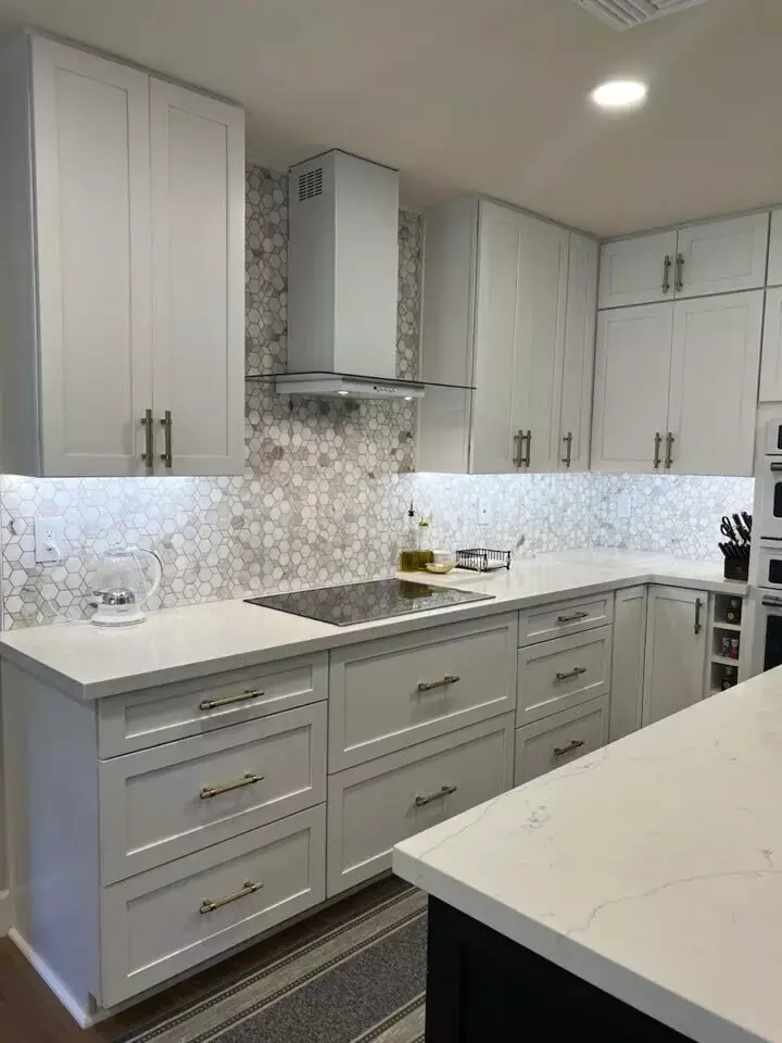 Contemporary kitchen featuring white shaker cabinets, gold hardware, a sleek glass cooktop, and a geometric tile backsplash.