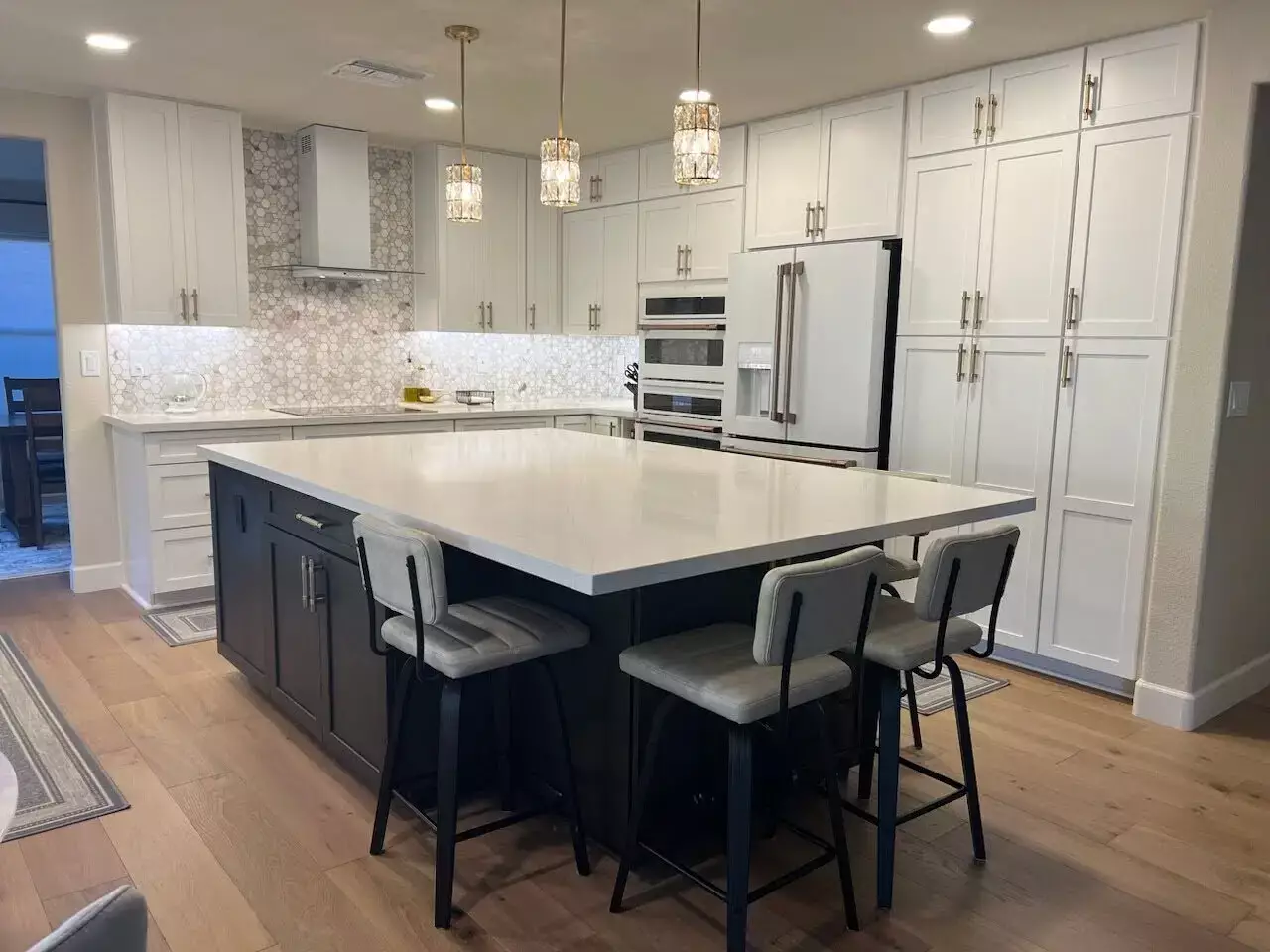 Modern kitchen with heated hardwood flooring, a large kitchen island, and white cabinetry, illuminated by pendant lights.