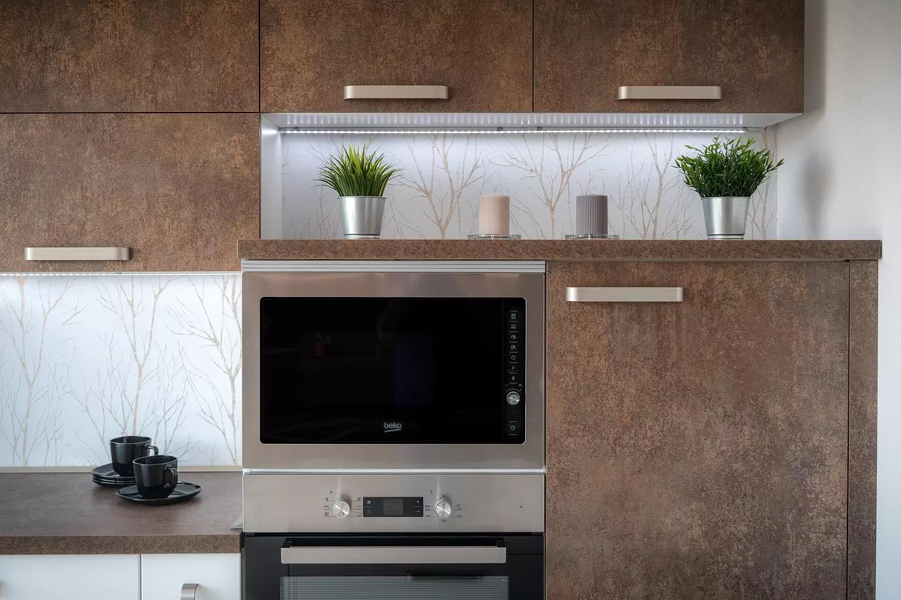 Modern kitchen with built-in stainless steel microwave and oven set against textured wooden cabinets, accented by decorative plants and candles.