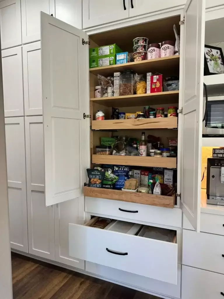 Modern kitchen pantry with pull-out wooden shelves and spacious drawers for organized food storage in a compact kitchen.