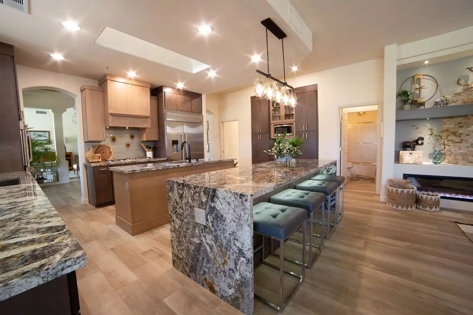 Modern open-concept kitchen with expansive granite island, sleek bar stools, mixed wood cabinetry, and efficient layout connecting to living space.