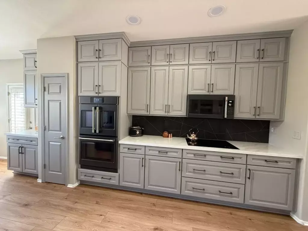 Modern galley kitchen in Phoenix featuring sleek gray cabinetry, black appliances, a dark geometric backsplash, and wood-style flooring.