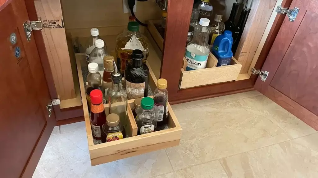 Pull-out cabinet drawers in a small kitchen neatly organizing bottles of oils, sauces, and household supplies for easy access.